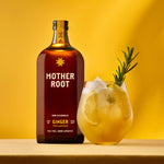 A bottle of Mother Root ginger beverage next to a glass filled with ice and ginger beverage, garnished with a rosemary sprig, on a yellow background.